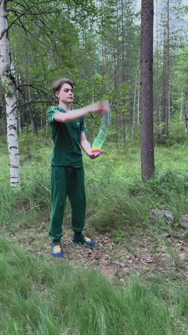 Young man in green athletic wear outdoors in a forest demonstrating springbending or slinky manipulation tricks with a Rainbow HyperSpring plastic spring toy