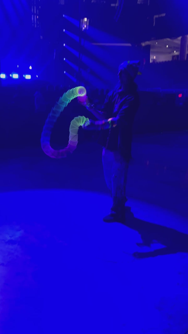 Flow arts performer under blue event lighting demonstrating springbending or slinky manipulation tricks with a glowing Rainbow HyperSpring plastic spring toy