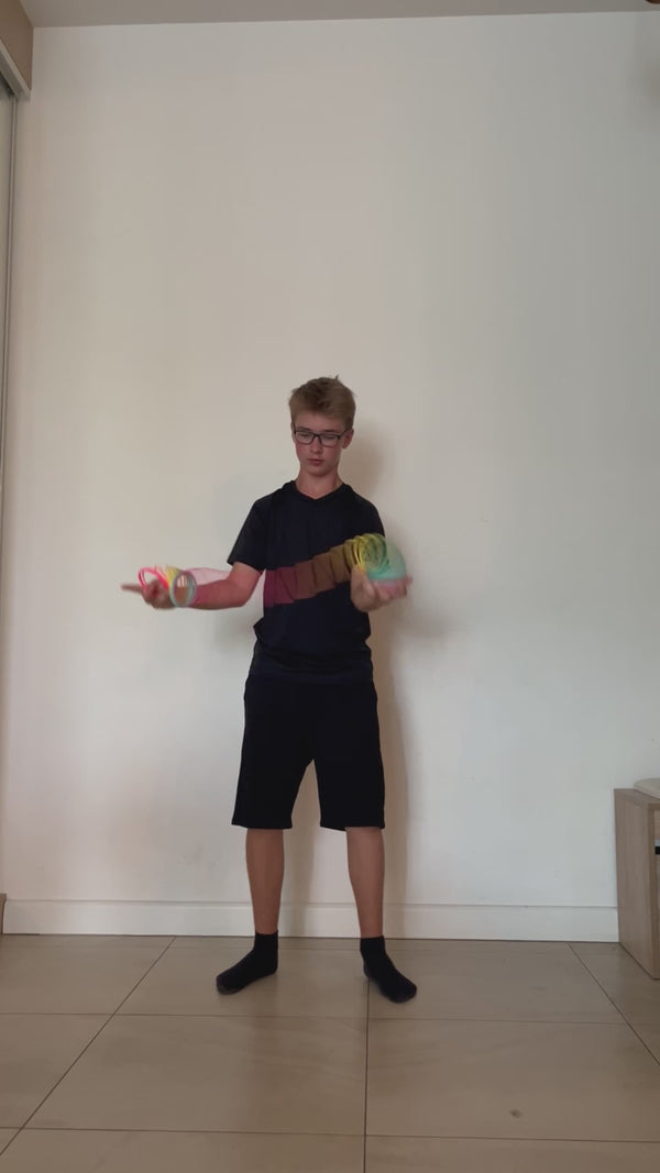 Young man wearing glasses indoors demonstrating springbending or slinky manipulation tricks with a Rainbow HyperSpring plastic spring toy