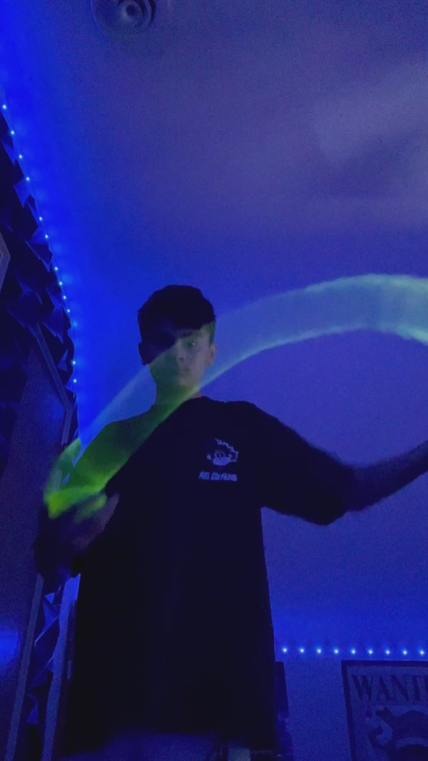 Young performer in a dark room illuminated by UV LED lights performing springbending or slinky manipulation tricks with a glowing Radioactive Yellow HyperSpring plastic spring toy
